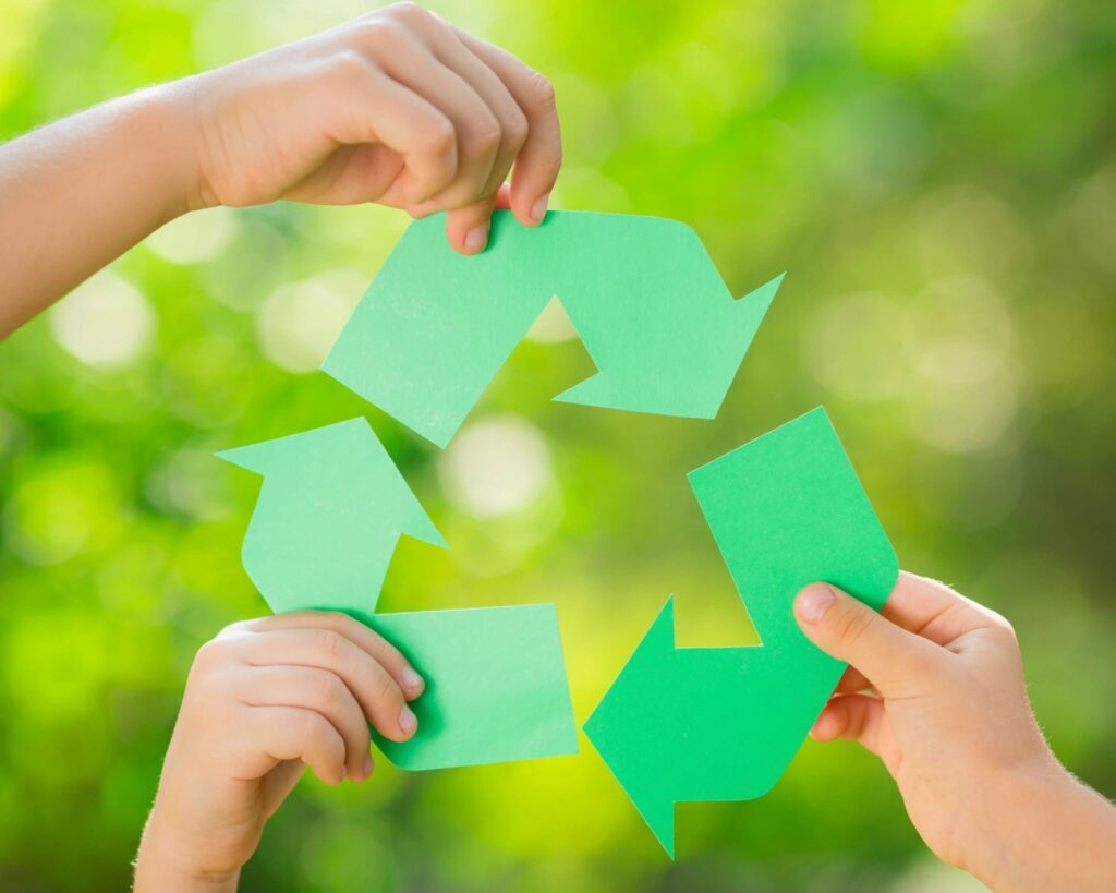 Four hands holding green paper to a recycling symbol.